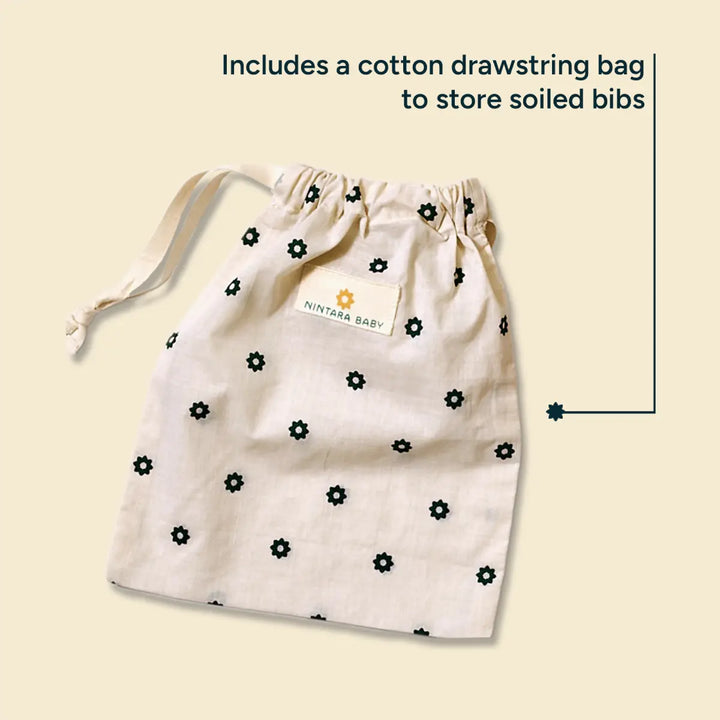 A neatly arranged cotton drawstring bag featuring the Nintara Baby logo and a delicate floral print. The bag is designed to store soiled bibs and other baby essentials, offering a practical, eco-friendly storage solution. Made from organic cotton, the bag features a soft yet durable texture. The muted, earthy tones of the design blend seamlessly with the natural fabric, while the drawstring closure ensures ease of use.