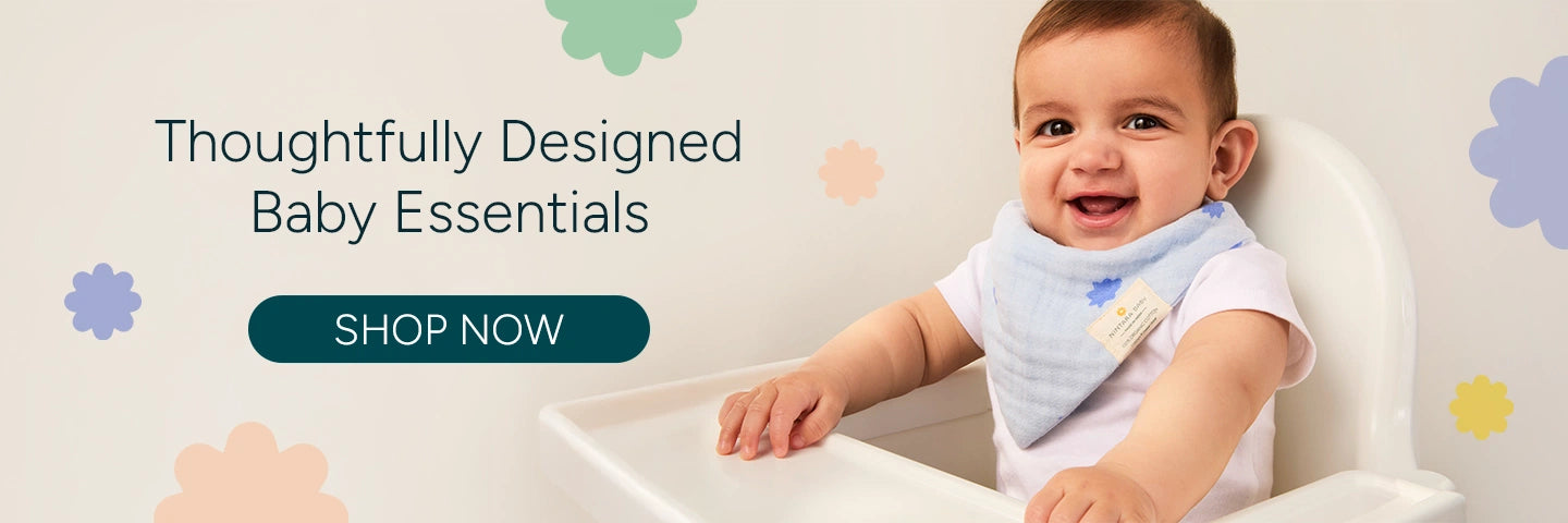 A smiling baby wearing a light blue bandana bib with floral designs, sitting in a highchair. The background features soft pastel flowers. The text 'Thoughtfully Designed Baby Essentials' is displayed next to the baby, with a call-to-action button saying 'SHOP NOW' in teal. The baby is enjoying the moment, adding to the friendly and nurturing vibe of the product image.