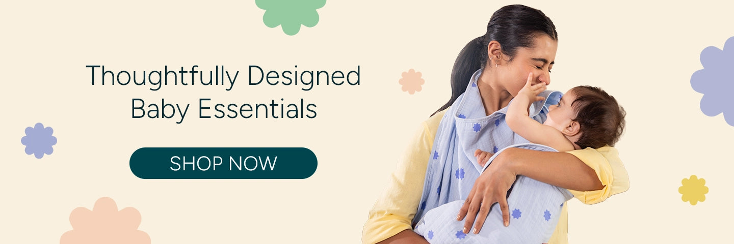 A mother lovingly wraps her baby in a soft muslin hooded towel featuring a blue stars print, holding the child close as they share a tender, joyful moment. She wears a light yellow outfit against a clean pastel background with playful floral shapes, alongside the text “Thoughtfully Designed Baby Essentials” and a prominent “Shop Now” call-to-action button.