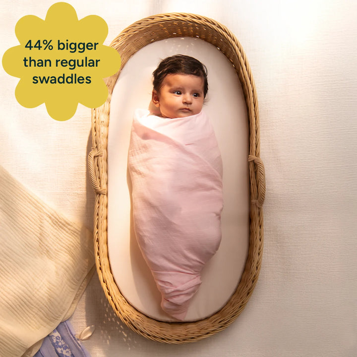 The baby is shown swaddled in a soft yellow swaddle, emphasizing the extra space it provides, being 44% larger than regular swaddles. The swaddle is gentle on the baby’s skin, made from organic, hypoallergenic muslin cotton to provide a safe and cozy environment for sleep.