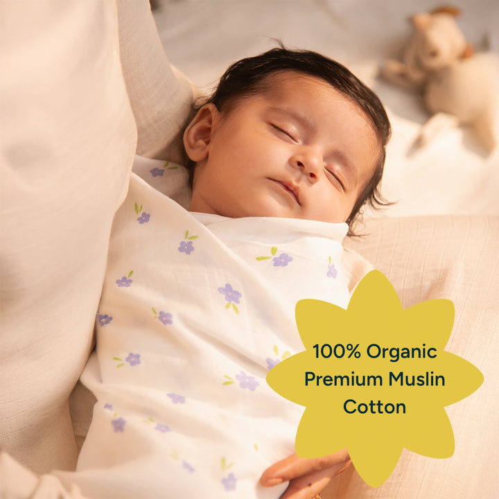 A baby, wrapped in a soft, pink swaddle, rests peacefully in a cozy basket. The 44% larger swaddle provides more room for the baby to move comfortably, with the design offering a secure, soft fit for a peaceful nap. The organic cotton material adds an extra layer of care and comfort for the baby's delicate skin.