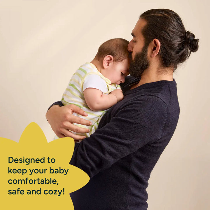 A parent lovingly holds their baby, both looking peaceful and content. The baby, wearing a striped green and white sleep sack, is being comforted in the parent’s arms. The image highlights the product's design to keep the baby comfortable, safe, and cozy, with the text 'Designed to keep your baby comfortable, safe and cozy!' placed on the left, symbolizing the nurturing and protective nature of the product.