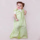 Cheerful baby on pink surface in Nintara Baby Forest Flutter sleep bag.White fabric with lime green dot and dash print, green piping trim, and tulip appliqué at zipper base.