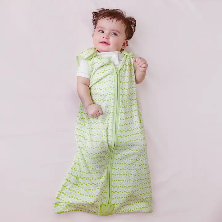 Cheerful baby on pink surface in Nintara Baby Forest Flutter sleep bag.White fabric with lime green dot and dash print, green piping trim, and tulip appliqué at zipper base.