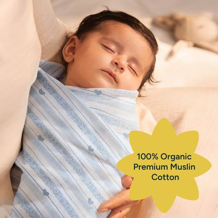 A peaceful infant swaddled in a soft, yellow organic cotton muslin swaddle, resting in the arms of a caregiver. The image showcases the premium quality of the fabric, emphasizing its breathability and softness. The baby is shown with their eyes closed, highlighting the comfort the swaddle provides. The alt text also includes a star-shaped label stating "100% Organic Premium Muslin Cotton," emphasizing the swaddle’s natural, eco-friendly material.