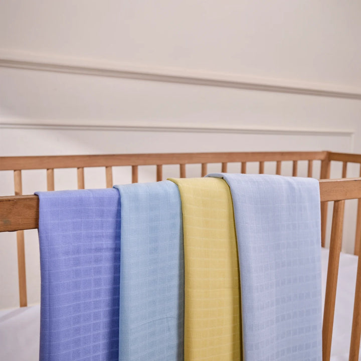Four pastel-colored baby blankets hanging over a wooden crib rail in a product image