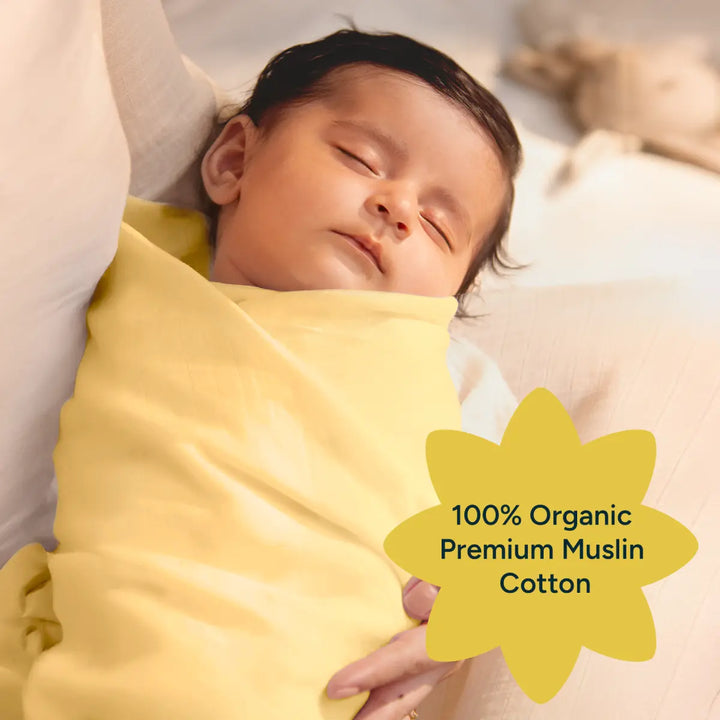 A peaceful infant swaddled in a soft, yellow organic cotton muslin swaddle, resting in the arms of a caregiver. The image showcases the premium quality of the fabric, emphasizing its breathability and softness. The baby is shown with their eyes closed, highlighting the comfort the swaddle provides. The alt text also includes a star-shaped label stating "100% Organic Premium Muslin Cotton," emphasizing the swaddle’s natural, eco-friendly material.