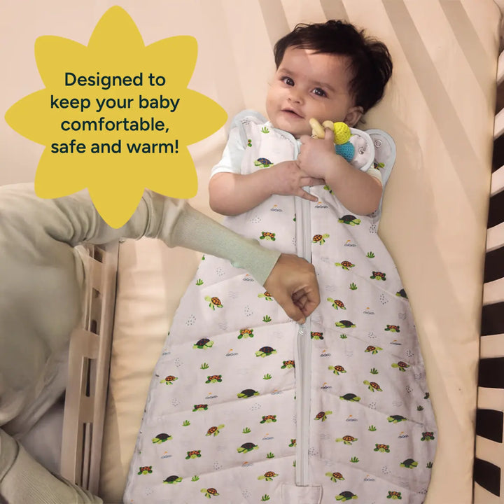 A cozy, soft baby sleep sack with a turtle and ladybug print is shown being gently zipped by a parent, ensuring the baby stays snug and warm. The baby, laying on a light beige mattress, holds a colorful teething ring with a joyful smile. The sleep sack's design is made of breathable, organic cotton to keep the baby comfortable. The background features a neutral tone, enhancing the focus on the baby's calm expression and the functional design of the sleep sack.