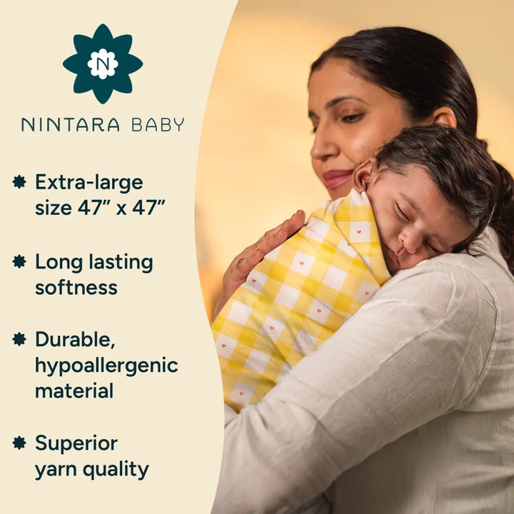 A mother cradles her baby, who is wrapped in a soft, yellow checkered swaddle made from organic cotton. The swaddle, with an extra-large size (47” x 47”), ensures the baby is swaddled comfortably. The fabric is soft, hypoallergenic, and durable, providing long-lasting softness unlike cotton-blend swaddles that lose softness over time.